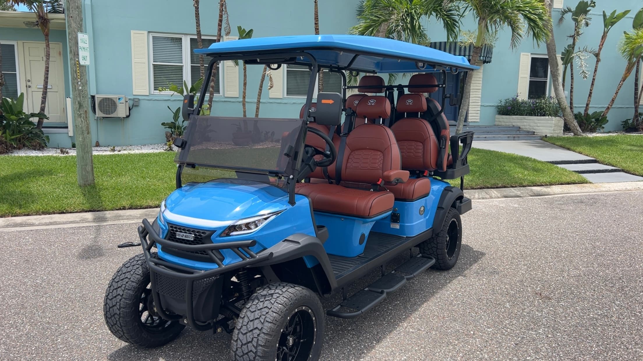 Azure-blue 2025 Venom EV 6-seater luxury golf cart with cognac leather seats parked on a Clearwater Beach street